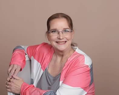 Smiling woman in a pink and gray cardigan, representing themes from Books That Reach Beyond Its Pages.